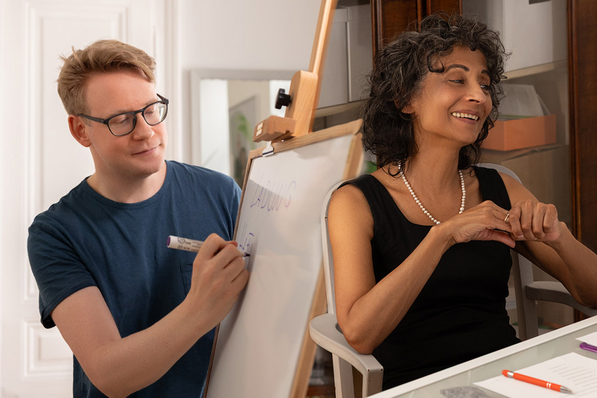 Michael En writing on a whiteboard; Michèle Cooke sitting at a table, smiling.